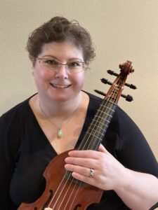 A woman with short brown hair in a black shirt holds a pardessus de viole.